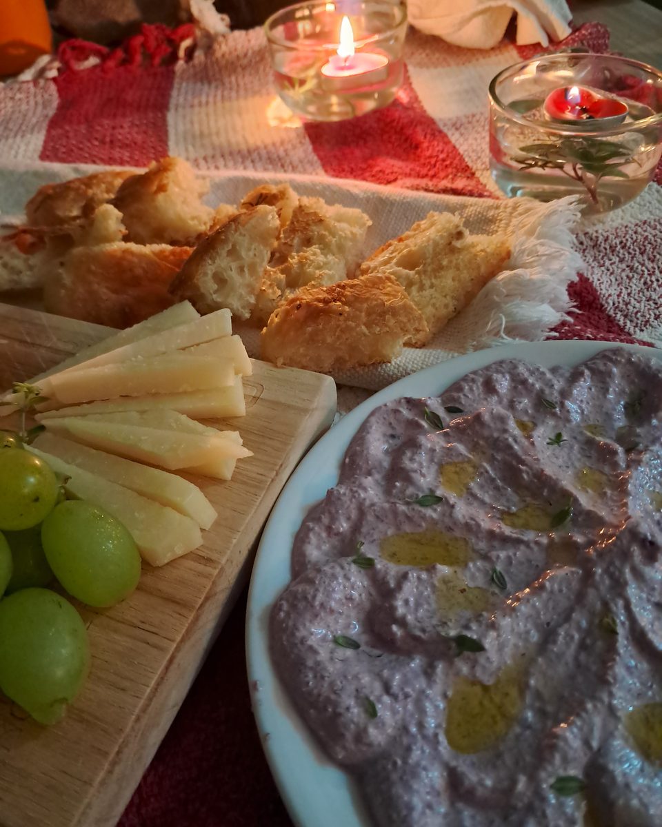 Mesa posta com patê, pão, queijo e uvas, à luz de velas.